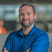 A smiling man with a beard and short dark hair in a blue polo shirt.